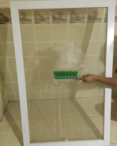 A screen is slathered with cleanser and a brush is scrubbing it.