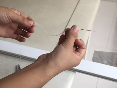 One is threading a straight needle with a piece of strong string.
